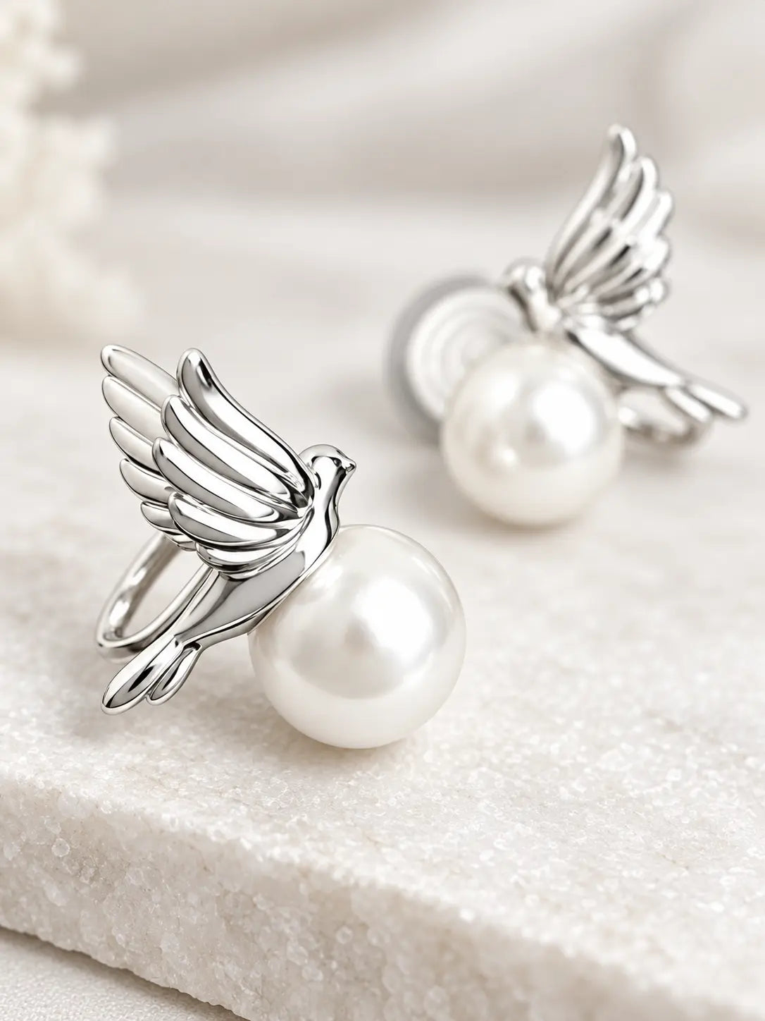 Close-up of Yeneast silver dove pearl stud earrings showing polished wings and lustrous pearl detail.