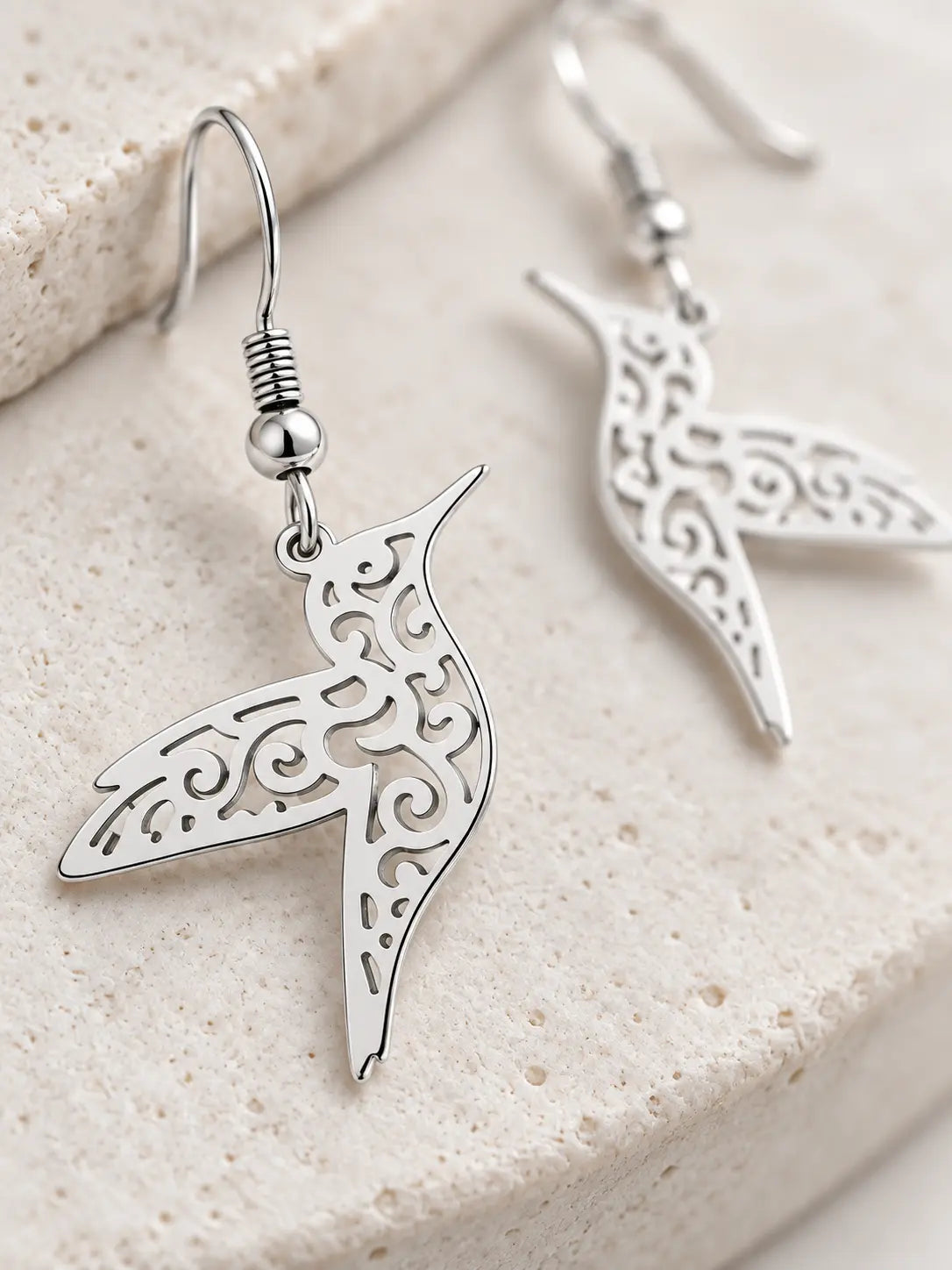 Close-up of Yeneast hummingbird earrings showing polished silver-tone finish and intricate filigree cutout craftsmanship.
