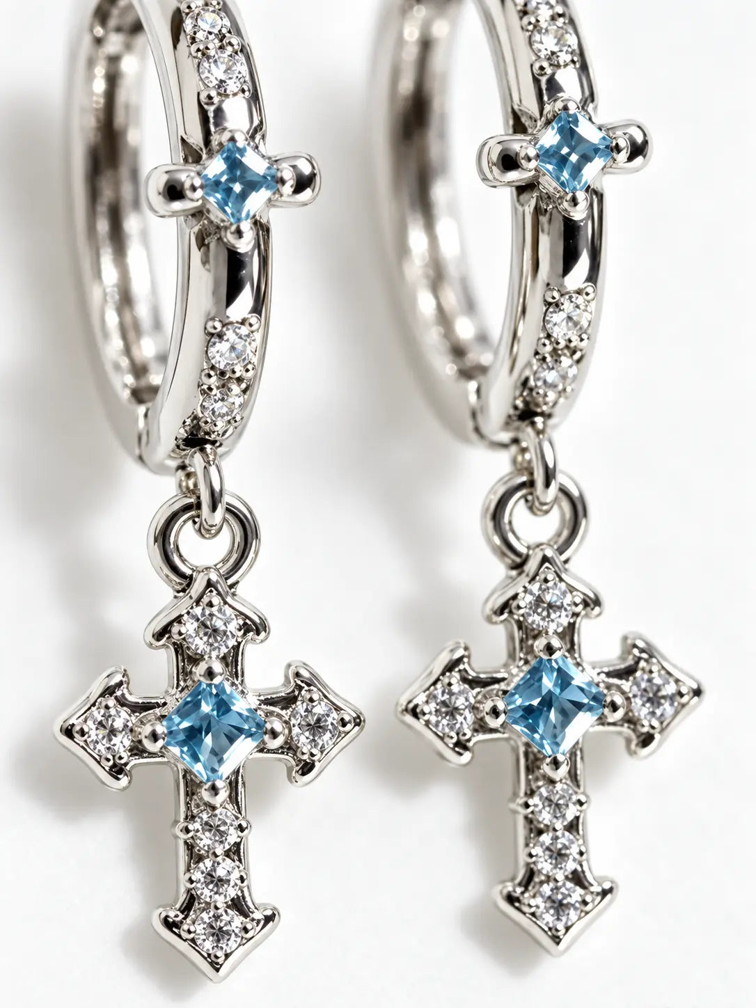 Close-up detail of YENEAST gemstone cross hoop earrings showing blue sapphire stones, pavé accents, polished silver finish and fine craftsmanship.