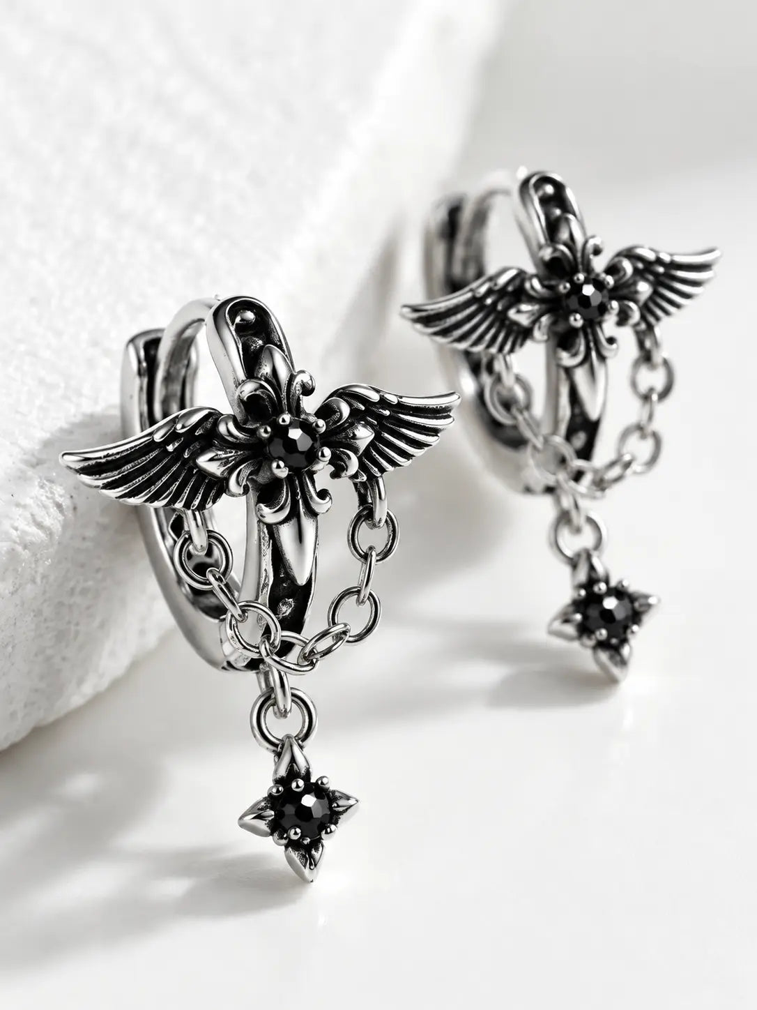 Close-up detail of YENEAST silver angel wing earrings showing layered feather texture, chain accents, polished metal and gemstone craftsmanship.