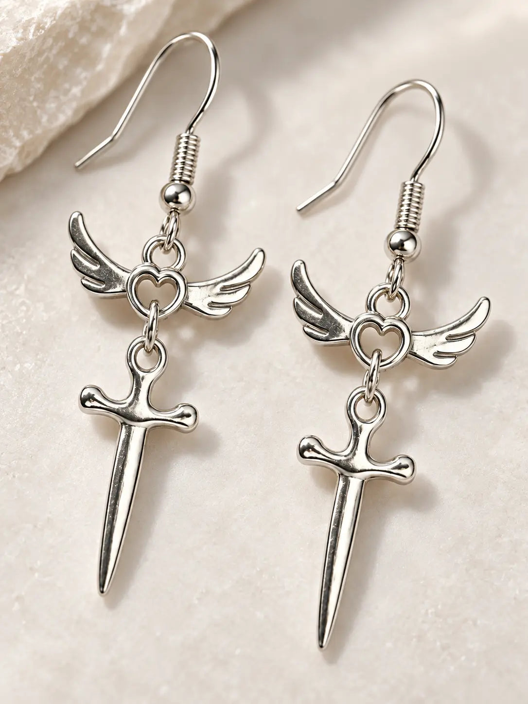 Close-up detail of YENEAST silver winged heart earrings showing polished metal finish, feather wing texture, heart charm and sword pendant craftsmanship.